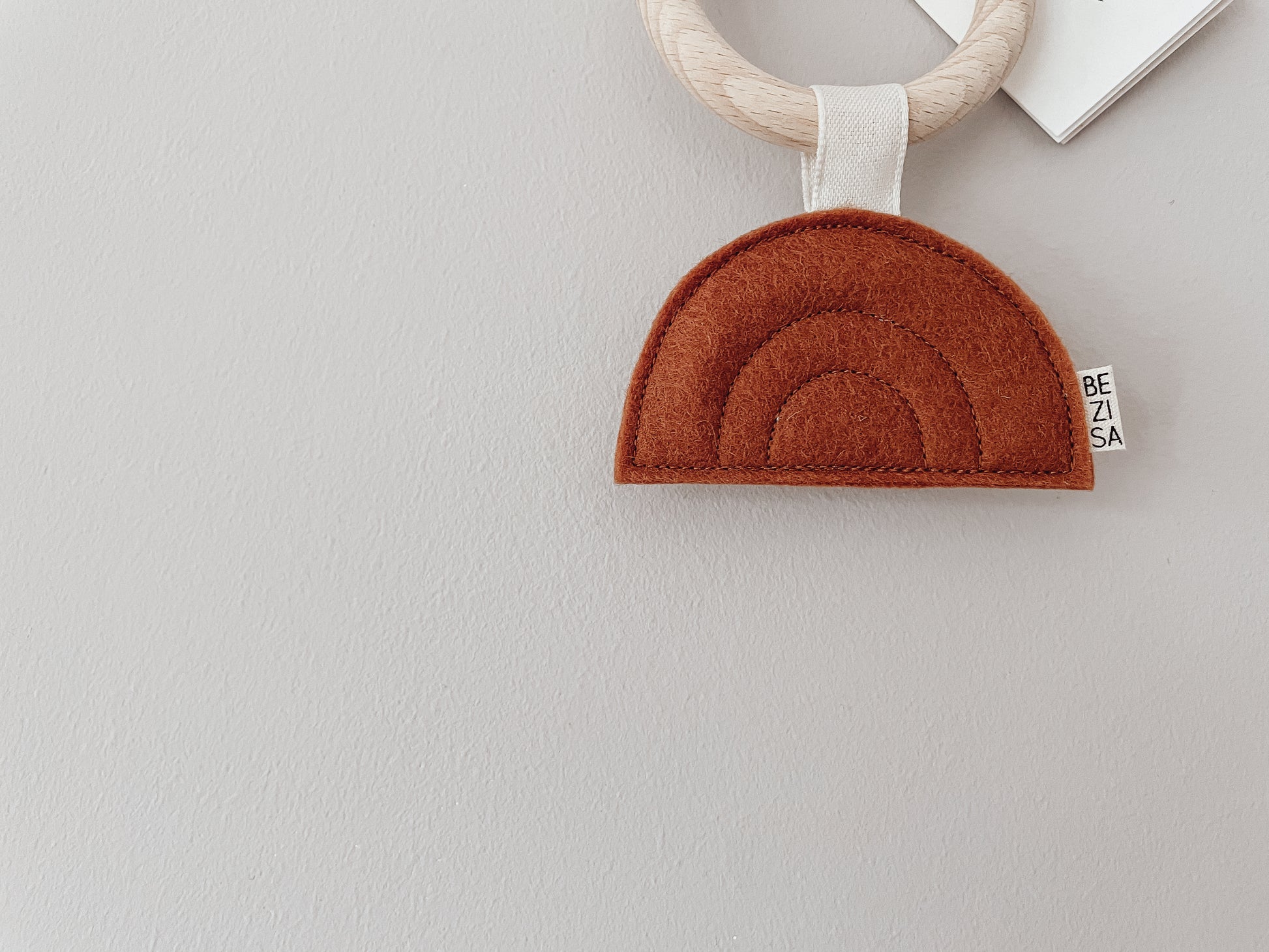 Bezisa Sunset teether in rust colour with wooden teething ring, photographed on a plain neutral background.