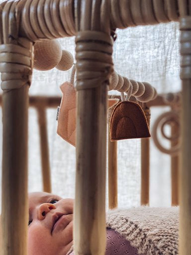 Bezisa Sunset felt rainbow shape hanging in a cot and baby is laying looking at the toys.