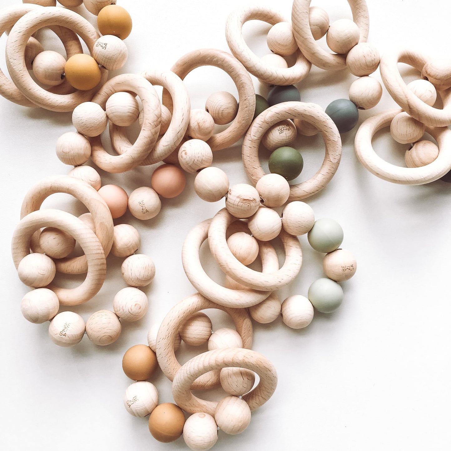 Bezisa wooden baby rattle with a mix of round wooden beads and coloured 100% silicone beads, plus two wooden rings. A selection of rattles photographed on a white background.