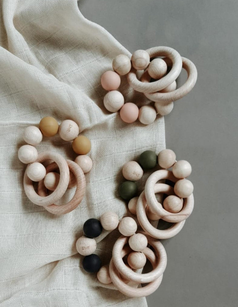 Bezisa wooden baby rattle with a mix of round wooden beads and coloured 100% silicone beads, plus two wooden rings. Four rattles photographed on a neutral muslin and background.