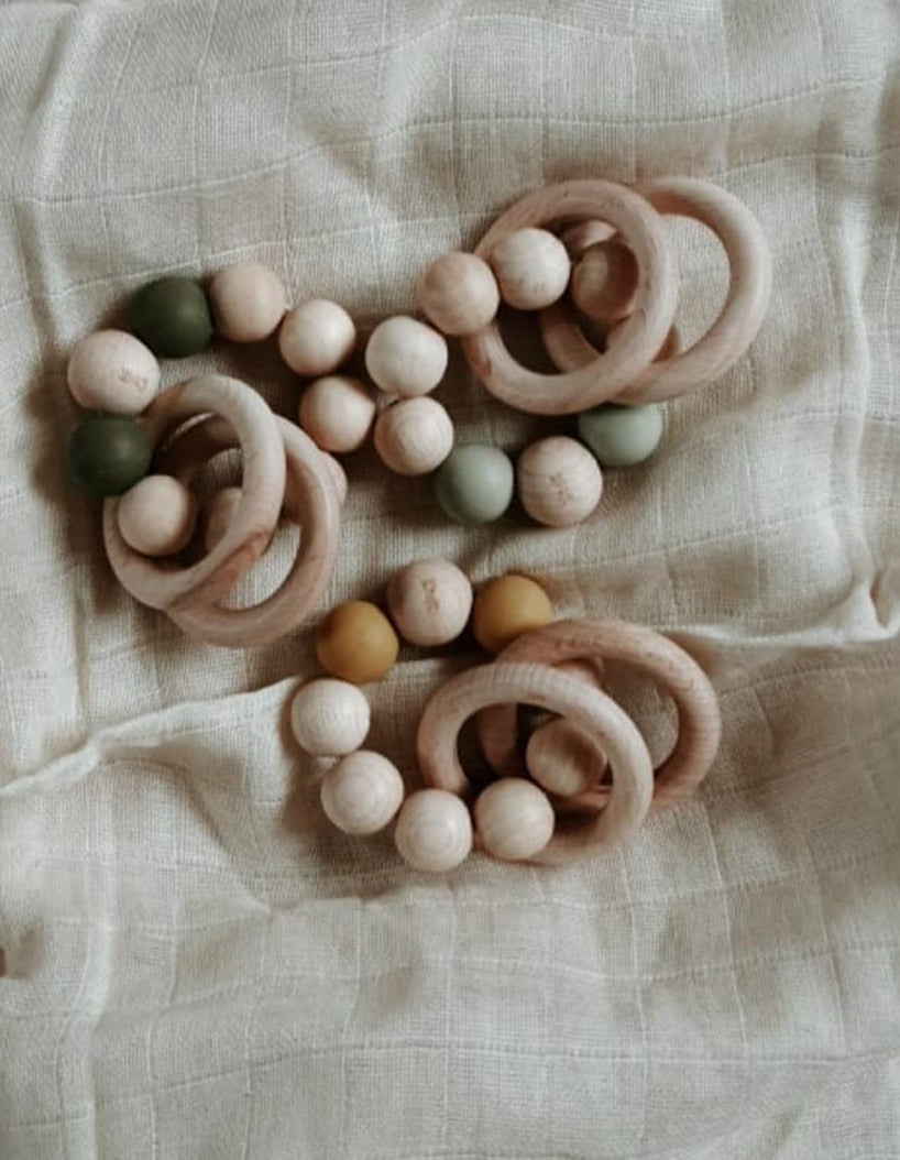 Bezisa wooden baby rattle with a mix of round wooden beads and coloured 100% silicone beads, plus two wooden rings. Three rattles are photographed on a neutral muslin.