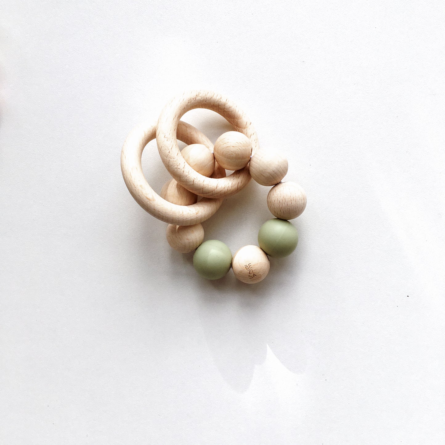 Bezisa wooden baby rattle with a mix of round wooden beads and pisatchio coloured 100% silicone beads, plus two wooden rings. Product is photographed on a plain white background.