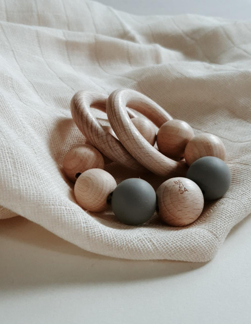 Bezisa wooden baby rattle with a mix of round wooden beads and stone coloured 100% silicone beads, plus two wooden rings. Product is photographed on a neutral muslin and neutral background.