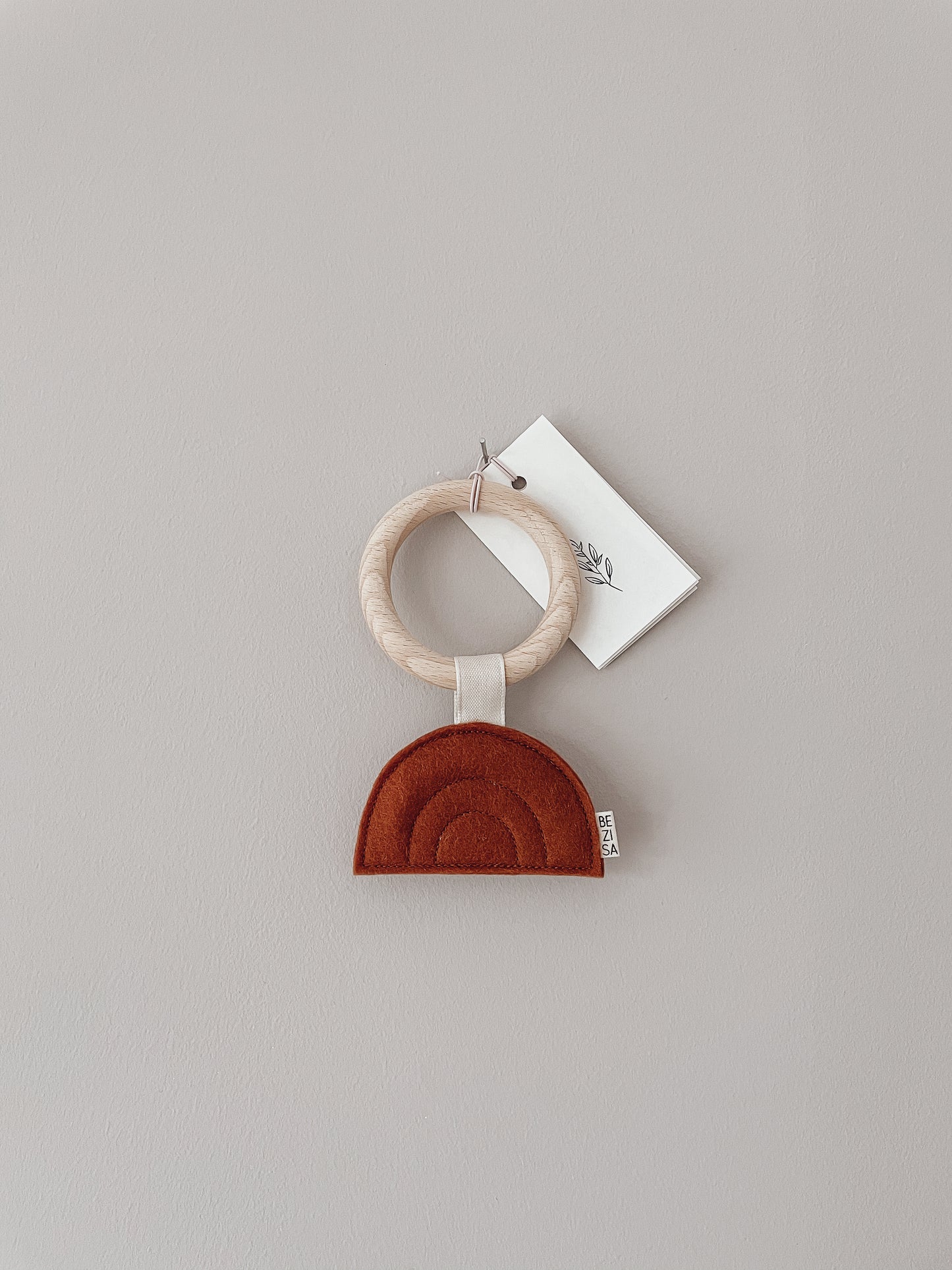 Bezisa Sunset teether in rust colour with wooden teething ring, photographed on a plain neutral background.