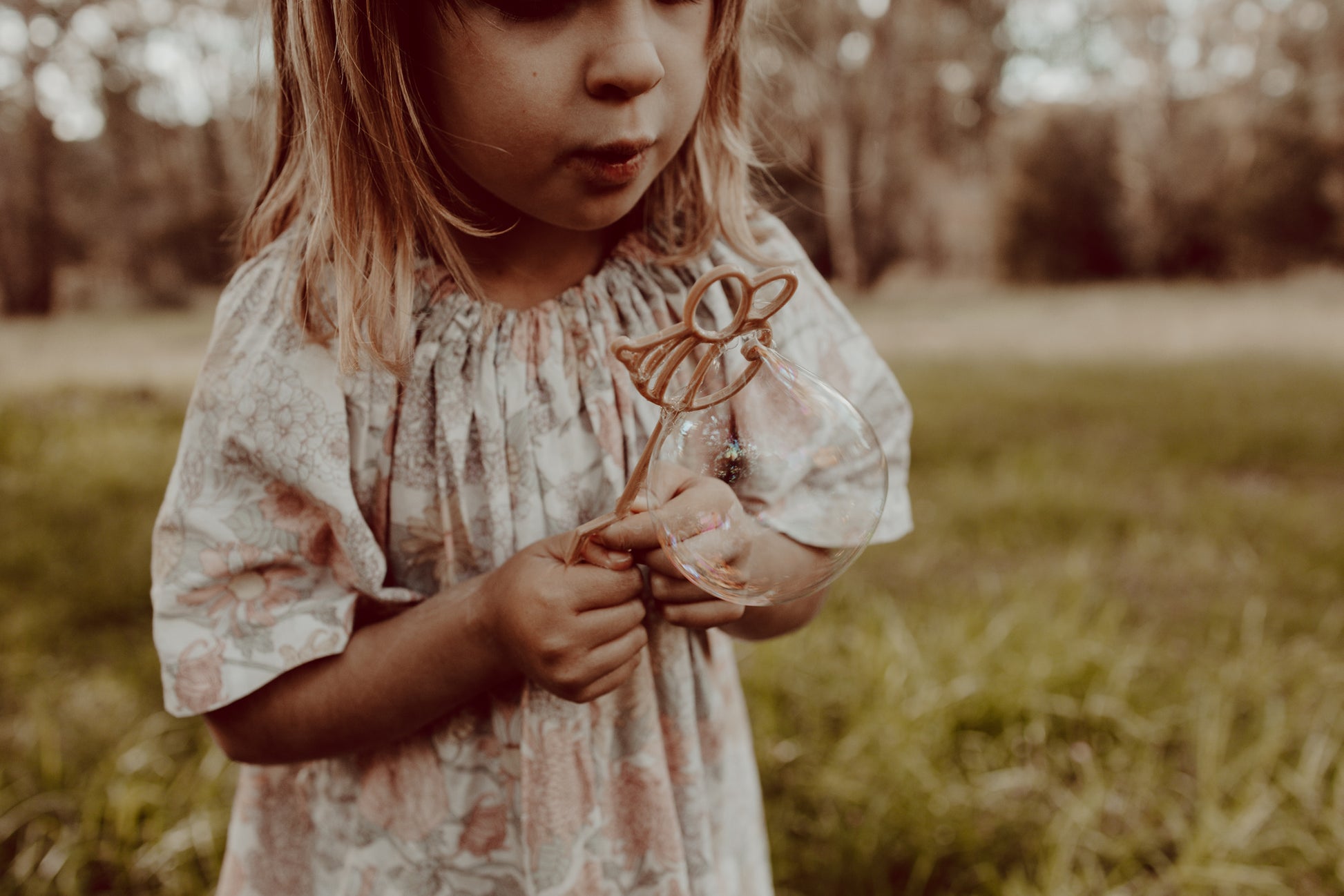 A little girl is blowing bubbles through the Kinfolk Pantry bee shaped eco bubble wand.