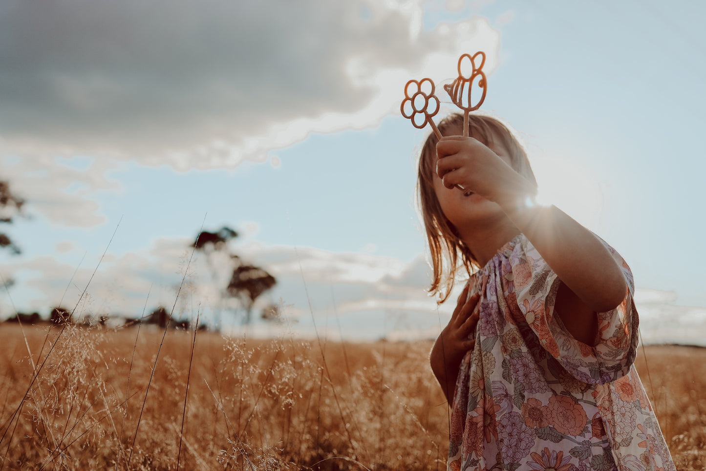 A little girl is holding the flower and bee shaped Kinfolk Pantry eco bubble wands as sun is shining on them.
