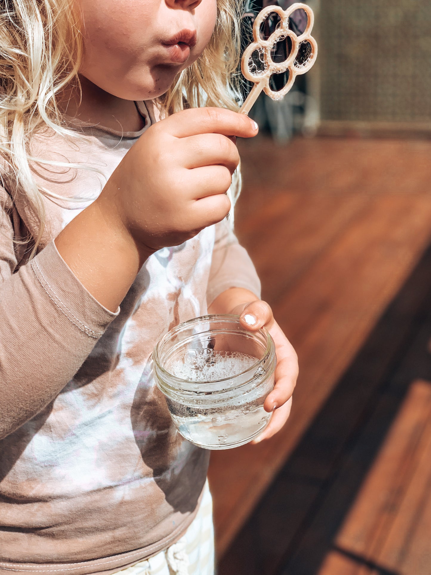 A little girl is blowing bubbles through the flower shaped Kinfolk Pantry eco bubble wand.