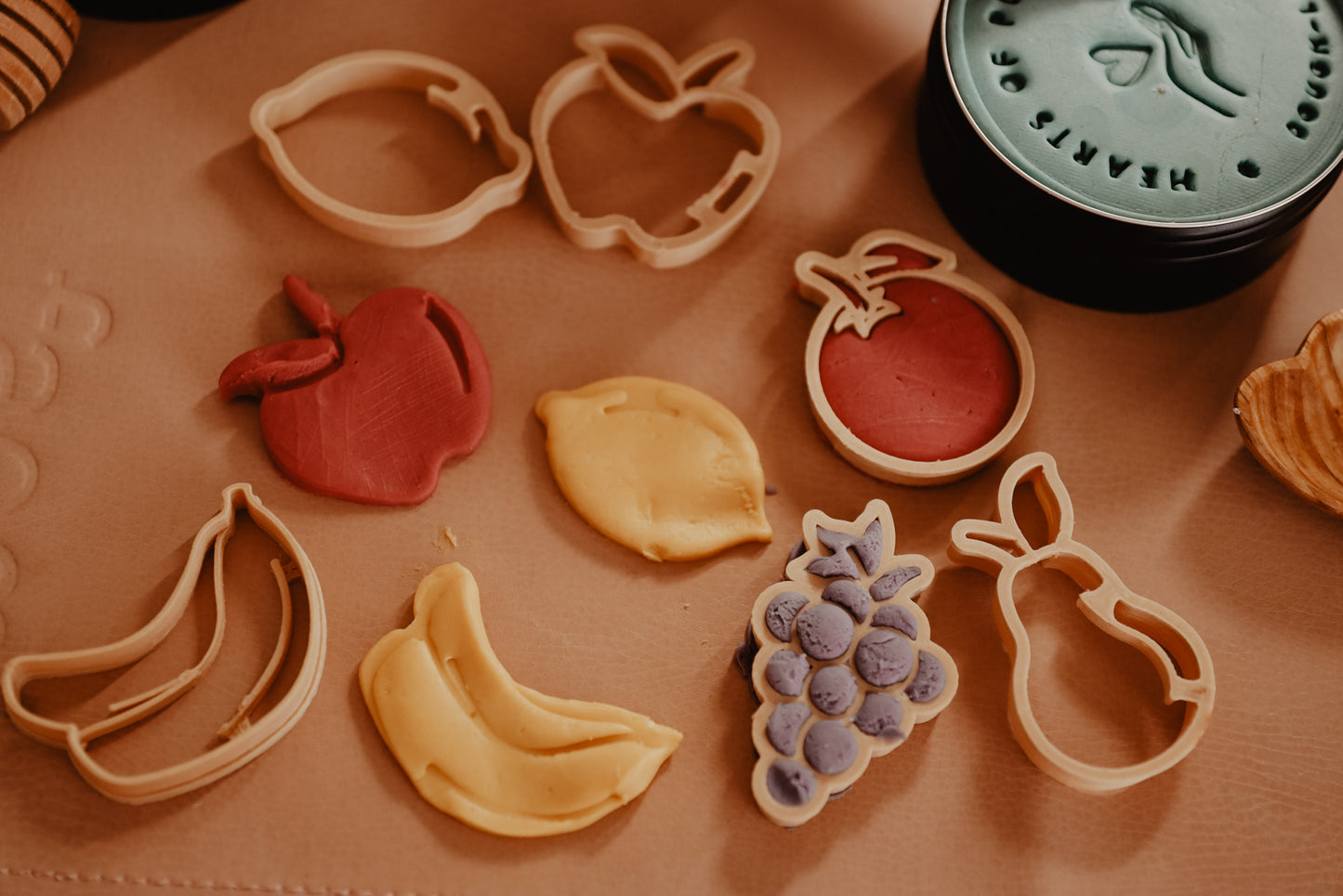Kinfolk Pantry set of 6 mini fruit eco cutters being used to cut shapes from playdough in orange, yellow and purple - great for sensory learning and play. Cutter set includes bananas, orange, apple, lemon, grapes and pear.