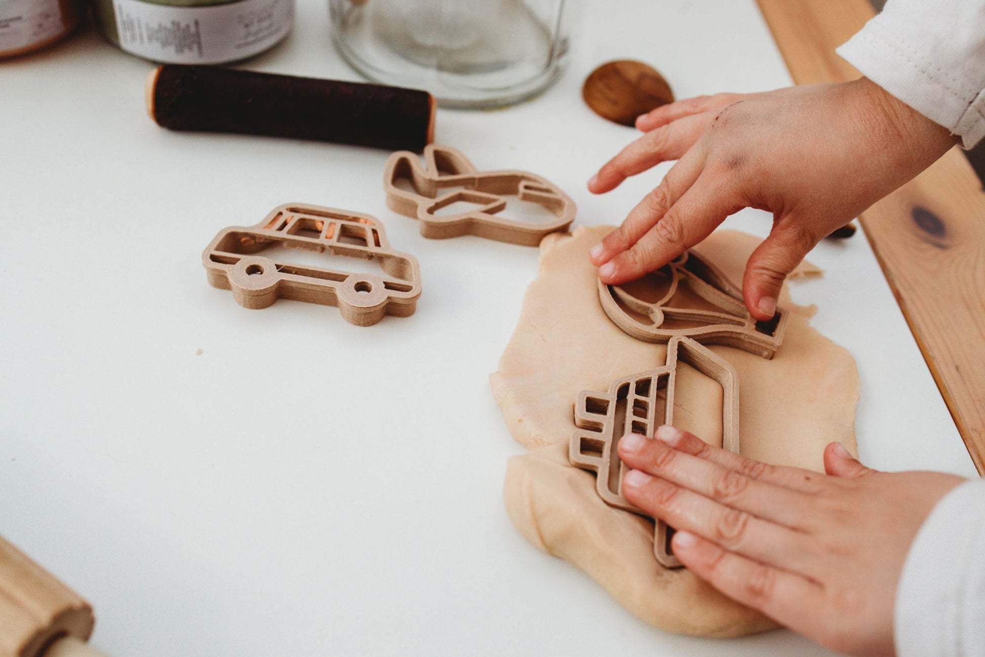 Kinfolk Pantry eco playdough cutters - a set of 6 transport themed biodegradable cutters for kids arts and crafts. Image shows a toddler using the cutters to make playdough shapes of the boat and hot air balloon with the car and plane cutters in the background.