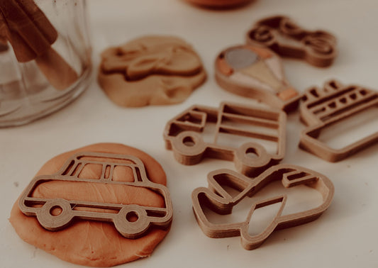 Kinfolk Pantry eco playdough cutters - a set of 6 transport themed biodegradable cutters for kids arts and crafts. Image shows the car cutter being used to make a shape in some orange playdough and the other cutter shapes blurred in the background.