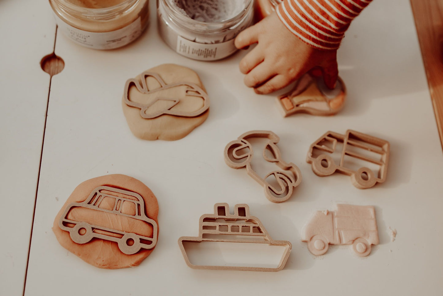 Kinfolk Pantry eco playdough cutters - a set of 6 transport themed biodegradable cutters for kids arts and crafts. Image shows a toddler using the cutters to make playdough shapes of the boat, plane, car, hot air balloon, motorbike and truck.