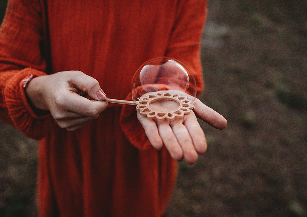 A girl in an orange dress holding the sunflower shaped eco bubble wand from Kinfolk Pantry - there is a large bubble that hasn't yet been popped!