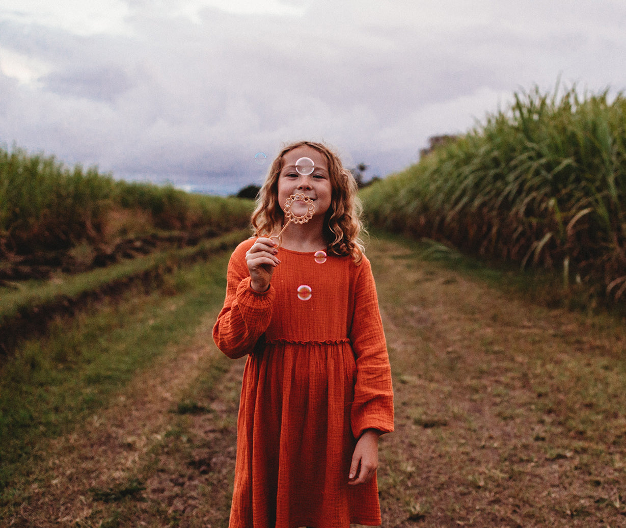 A girl in an orange dress holding the sunflower shaped eco bubble wand from Kinfolk Pantry - there are a few bubble that haven't yet been popped!
