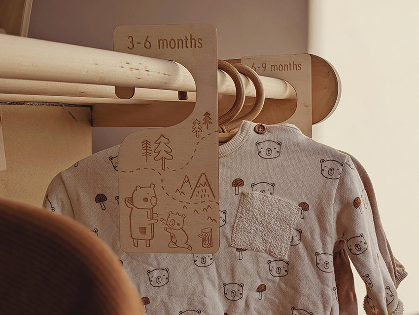 Bear illustrations and woodland design laser cut onto plywood for these baby clothing dividers by Paper & Bean, perfect as a baby shower gift ready for a newborn. Clothing dividers in this image are hung on a wooden rail with baby clothing in neutral colours.